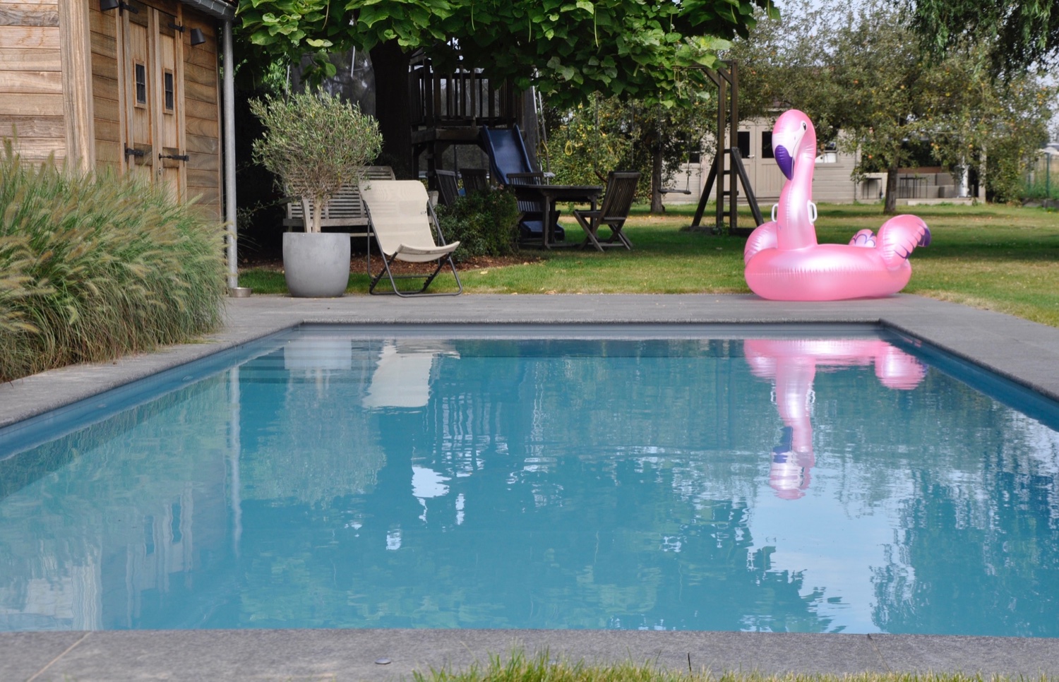 roze flamingo licht naast een lichtgrijs zwembad met rolluikplage en trap